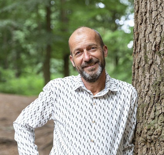 Reinier van den Berg, meteorologist and speaker, leaning against a tree in the forest